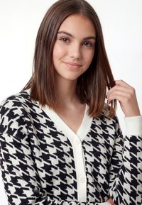 Zwart-witte pied-de-poule cardigan met een V-hals, voorzien van knoopsluiting en geribde boorden. Zachte textuur, lichtgewicht materiaal.
