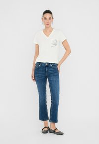 Camiseta blanca de cuello en V con un detalle de bolsillo de estampado de leopardo, combinada con jeans de pierna recta de color azul oscuro y bailarinas negras con estampado.