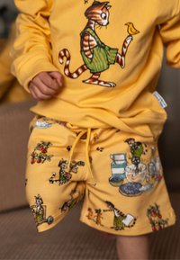 Gelb cotton Outfit mit einem grafischen Kater auf dem Shirt und verspielten Mustern auf den Shorts, einschließlich Nahrungsmitteln und Charakteren.