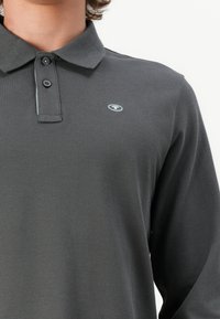 Tumehall pikkade varrukatega polo-särk, mis on valmistatud tekstuuri kangast. Omab kolme nupuga plikaati ja väikest logo vasakul rinnal.