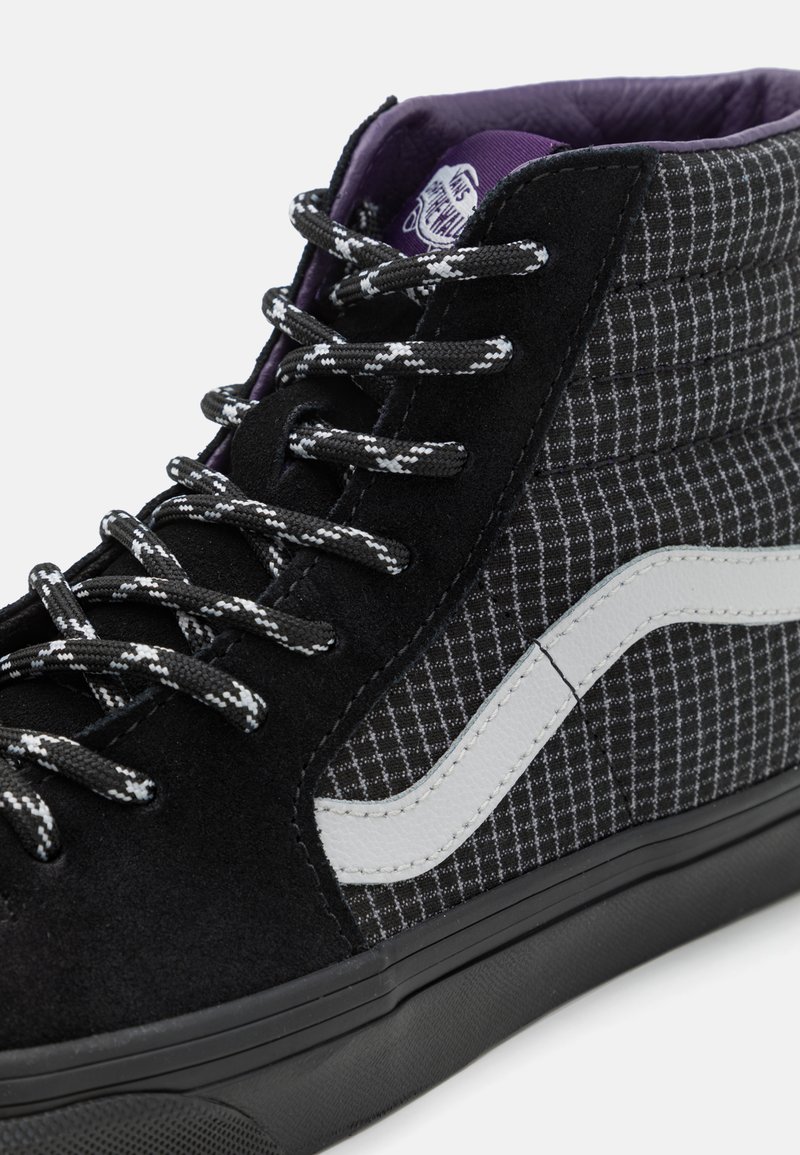 Sneaker alto in nero e grigio con motivo a scacchi, materiali in suede e tela, lacci neri e striscia laterale in pelle bianca.