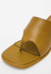Brown synthetic slide sandal with an open toe design, thick strap, and smooth, matte texture. Flat sole with rounded edges.