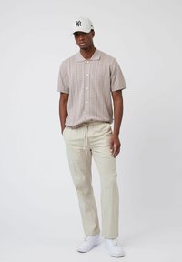 Polo shirt en tricot beige clair avec un motif texturé, associé à un pantalon à cordon de couleur crème et des baskets blanches. Casquette de baseball incluse.