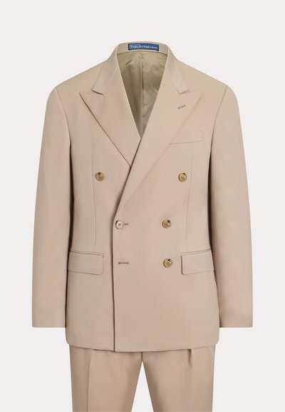 Giacca da completo doppiopetto beige con sei bottoni, rever a punta e tasche con patta, abbinata a pantaloni coordinati su sfondo semplice.