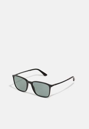 Lunettes de soleil carrées noires avec verres verts, monture en plastique léger et accents en métal épurés sur les branches. Design minimaliste.