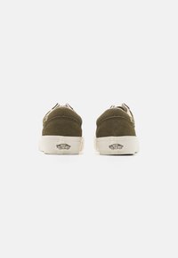 Zapatillas de ante verde oliva con suelas de goma blanca. Presentan detalles de costura y un logo en el talón. Diseño bajo con forma redondeada.