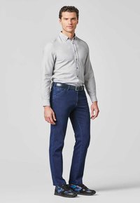 Graues Hemd mit Knopfleiste, dunkelblaue Jeans und schwarze Sneakers mit blauen Akzenten. Glattes Material mit geradem Schnitt. Keine sichtbaren Muster.