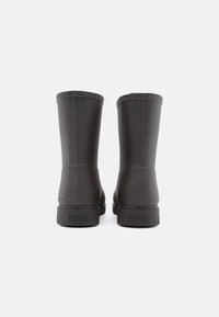 Tmavě hnědé gumové deštné boty s hladkým povrchem, rovnou siluetou horní části a jemným logem na patě, které mají zaoblený horní okraj.