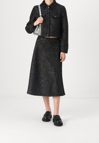 Musta tweed-takki ja siihen sopiva midi-hame, jossa on tekstuuripinta. Korostettuna metallilangalla, yhdistettynä mustiin liukuvaan kenkiin.