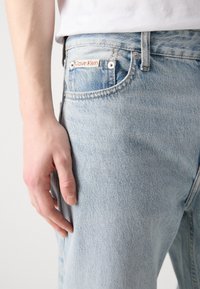 Svetle modré džínové kalhoty s vybledlým vzhledem, pětikusový design a nášivka s logem Calvin Klein na přední kapse.