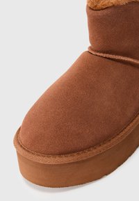 Brune semsket vinterstøvel med tykk gummisåle og rund tå, med en myk, varm fôr som er synlig ved den øvre kanten.