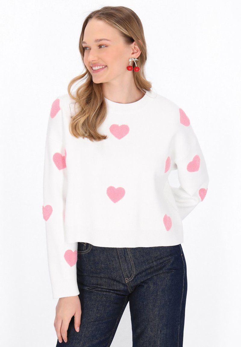 Pulover alb tricotat cu modele de inimi pufoase roz, decolteu rotund și mâneci lungi. Asortat cu blugi negri.