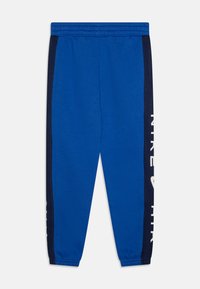Blå sportiga sweatpants med marinblå sidremsor och vitt tryck. Elastisk midja och ribbade muddar. Tillverkade av mjukt, stretchigt tyg.