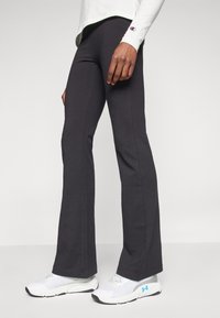 Czarne legginsy dzwonowe z elastycznej tkaniny. Charakteryzują się gładką teksturą i zestawione są z białymi butami sportowymi z niebieskimi akcentami.