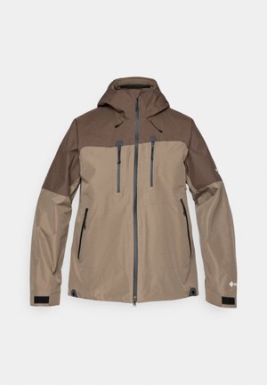 Ruskea ja beige vedenpitävä takki hupulla, vetoketjukiinnitys edessä ja useita vetoketjullisia taskuja. Sisältää tekstuurin olkapaneelin ja säädettävät hihansuut.