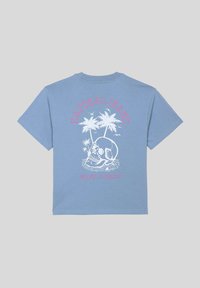 T-shirt en coton bleu clair avec un graphisme de crâne et de palmiers en blanc, accompagnés des inscriptions "KAPORAL JEANS" et "RELAX & ENJOY" en texte rose.