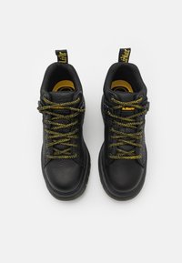 Botas de caminhada em couro preto apresentam uma biqueira redonda, parte superior texturizada, detalhes em amarelo e grossas, atacadas, fitas de sapato dourado-esverdeadas.