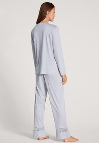 Lichtblauw pyjama set gemaakt van zachte stof; lange mouwen top en losse broek met kantaccenten aan de onderkant.