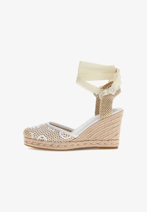 Espadrille compensée beige avec texture tissée, bout en mesh blanc à motifs, et rubans crème à la cheville noués en nœud.