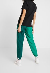 Černé tričko s krátkým rukávem v kombinaci se zelenými zúženými kalhotami. Kalhoty mají elastické manžety a malou detalní nášivku. Bílá sneakers dotvářejí celkový vzhled.