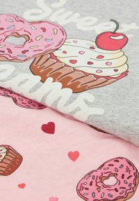 Šedá látka s karikaturami donutů a jednoho cupcake, obsahující barvy jako růžová, červená a hnědá. Doplněná srdíčky a stylizovaným textem.