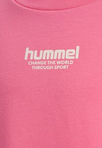 Tissu rose avec texte blanc "hummel CHANGE THE WORLD THROUGH SPORT" centré sous un col arrondi.