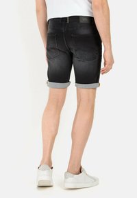 Jeansshorts in verblasstem Schwarz mit umgeschlagenem Saum. Verfügt über ein Fünf-Taschen-Design und ein Etikett am Bund. Kombiniert mit weißen Sneakern.