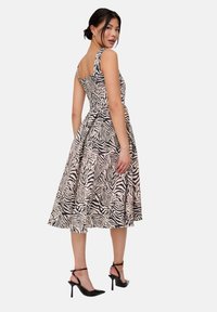 Kleid mit Zebramuster in Schwarz und Beige, mit tailliertem Oberteil und ausgestelltem Rock, kombiniert mit schwarzen Sandalen mit hohen Absätzen.