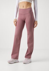 Pantaloni elasticizzati rosa chiaro con vita alta e logo Nike nero. Il tessuto è liscio con una silhouette aderente e gambe a campana.