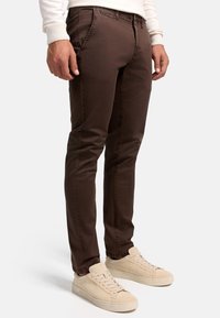 Pantalones slim-fit marrones hechos de una tela texturada, que presentan un diseño clásico de cinco bolsillos con costuras visibles y cremallera.