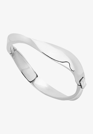 Srebrna metalowa bransoletka o gładkim, zakrzywionym wzorze. Posiada polerowane wykończenie i subtelny wzór fal, ukazując jednoczęściową sylwetkę.