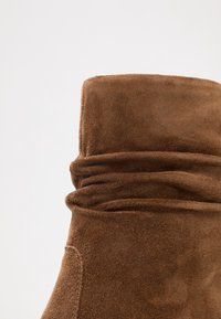 Bruine suede laars met een slouchy ontwerp, voorzien van een zachte textuur en een gevouwen manchet. De nadruk ligt op de rijke kleur en de gladde afwerkingsdetails.