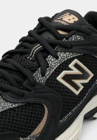 Sapatilha de corrida New Balance preta com tecido em malha, detalhes com padrão, atacadores pretos espessos e sola branca.