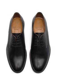 Scarpe in pelle nera con punte arrotondate, design con lacci, texture liscia e una finitura leggermente lucida. La fodera interna presenta un dettaglio del marchio.