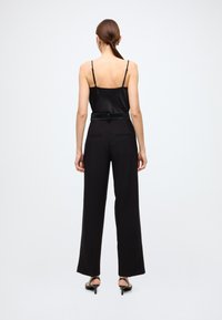 Črna satenasta majica s tankimi naramnicami, združena s črnimi hlačami z visokim pasom. Hlače imajo zadnje žepe in širok kroj nogavic.