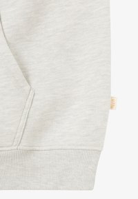 Helle graue Sweatshirt aus strukturiertem Stoff, mit einer Fronttasche, gerippten Bündchen und einem kleinen Etikett an der Seite eingearbeitet.