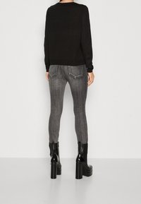 Schwarzes Langarmoberteil kombiniert mit engen grauen Jeans. Die Jeans haben eine dezente vertikale Textur und zwei Gesäßtaschen. Abgerundet mit klobigen schwarzen Stiefeln.