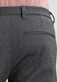 Grå texturerade byxor med slim fit, med en enda bakficka och en synlig midjebandstapp, tillsammans med en ljusrosa rutigt skjorta.