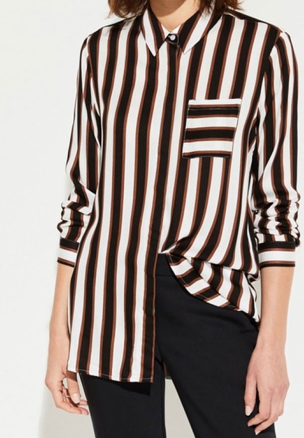 Femme portant une chemise à manches longues boutonnée avec des rayures verticales noires, blanches et marron et une poche poitrine rayée assortie.