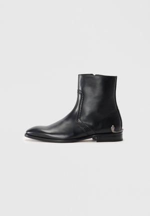 Black leather ankle boot with pointed toe, textured side detail, low heel, and a small decorative silver snake accent on the heel.