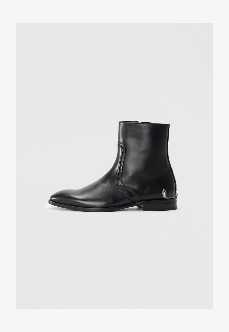 Bottine en cuir noir à bout pointu, avec un détail latéral texturé, un petit talon et un accent décoratif en argent en forme de serpent sur le talon.