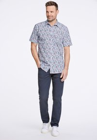 Camicia a maniche corte con bottoni, decorata con un motivo floreale blu, abbinata a pantaloni blu scuro e sneakers bianche. La camicia ha una vestibilità comoda e colletto.