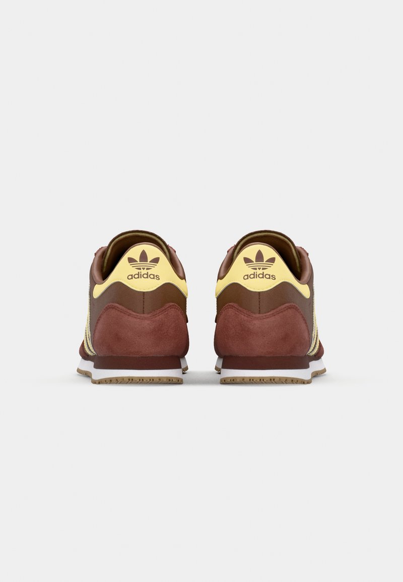 Adidas sneakers med en maroon ruskindsoverdel, gule accenter og en hvid mellemsål, med et klassisk tre-strips design og struktureret hæl.