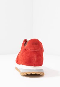 Punaiset mokkanahkakengät, joissa on valkoinen keskiosa ja kuminen ulkopohja, pyöreä muoto ja hienovaraiset ompeluyksityiskohdat kantapäällä.