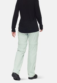 Ljusgröna byxor med avtagbara ben i en mjuk struktur, med snedställda fickor och resår i midjan, tillsammans med en svart långärmad topp.