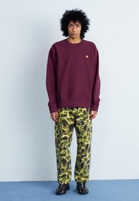 Vínová mikina se žebrovanými manžetami, kombinovaná s volnými zelenými maskáčovými kalhotami s černými akcenty. Outfit doplňují černé boty.