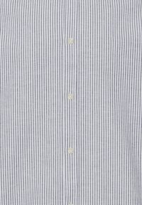 Chemise à boutons présente des rayures verticales bleu marine et blanches. Fabriquée en tissu léger avec une surface texturée et six boutons ronds.
