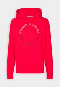 Red hoodie with a kangaroo pocket, featuring circular "TOMMY HILFIGER NEW YORK CITY" logo in contrasting colors. Soft fabric and elastic cuffs.