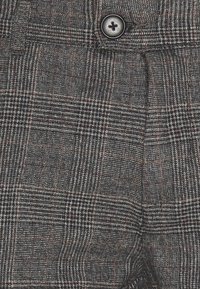 Grijze geruite broek met een gestructureerde stof en een knoopdetail op de tailleband, benadrukt door dunne rode en witte lijnen.