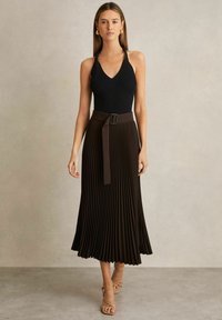 Top senza maniche nero a coste abbinato a una gonna marrone plissettata con vita con cintura. Sandali con cinturini sottili completano il look.